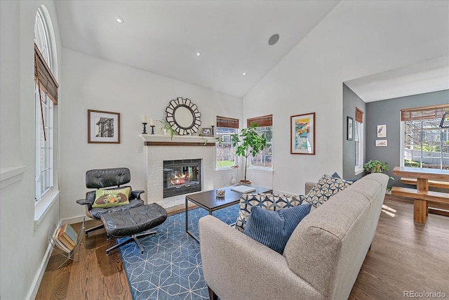 living area featuring wood finished floors, a glass covered fireplace, high vaulted ceiling, baseboards, and recessed lighting