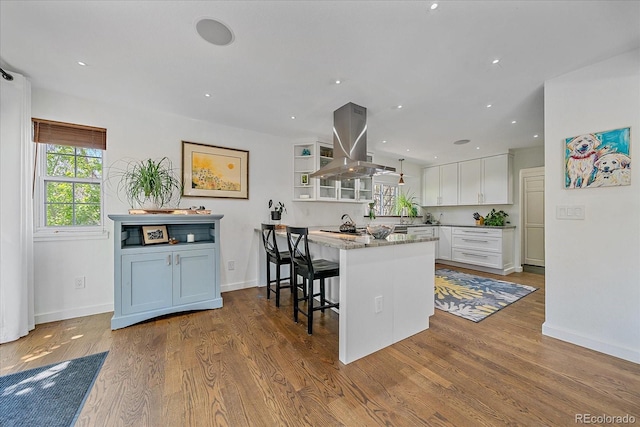 kitchen featuring island exhaust hood, white cabinets, a kitchen breakfast bar, baseboards, and recessed lighting