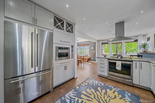 kitchen with appliances with stainless steel finishes, island exhaust hood, wood finished floors, recessed lighting, and baseboards