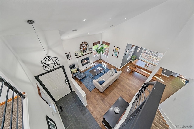 living room with high vaulted ceiling, stairway, wood finished floors, a glass covered fireplace, and baseboards