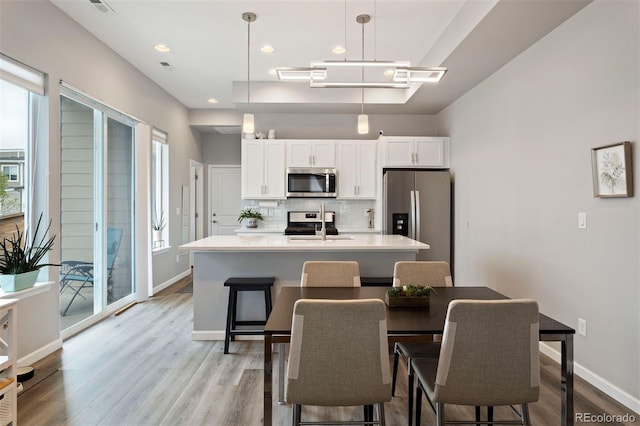 kitchen with appliances with stainless steel finishes, decorative light fixtures, white cabinetry, and a kitchen island with sink