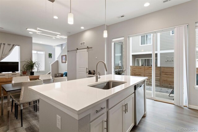 kitchen with sink, a barn door, stainless steel dishwasher, pendant lighting, and a center island with sink