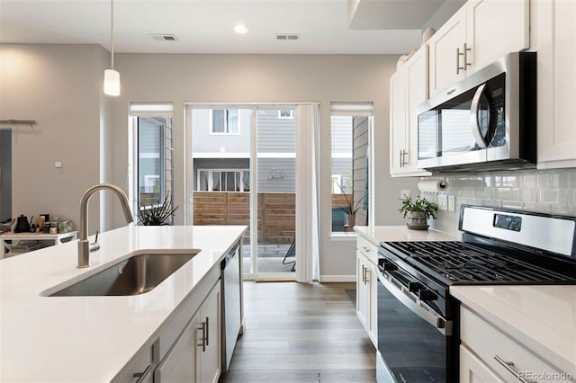 kitchen featuring white cabinetry, sink, stainless steel appliances, and decorative light fixtures