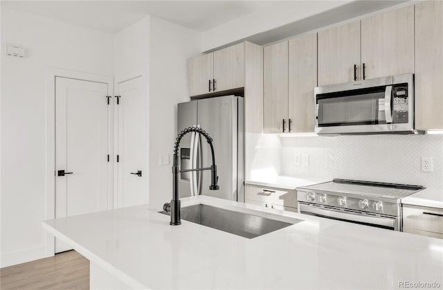 kitchen featuring appliances with stainless steel finishes, backsplash, light brown cabinetry, and sink