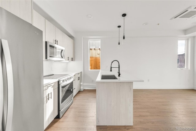 kitchen with stainless steel appliances, sink, pendant lighting, light hardwood / wood-style floors, and an island with sink