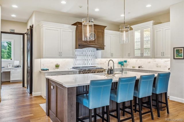 kitchen with an island with sink, glass insert cabinets, a kitchen breakfast bar, light countertops, and white cabinetry