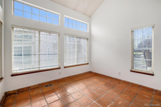 spare room featuring high vaulted ceiling, tile floors, and a textured ceiling