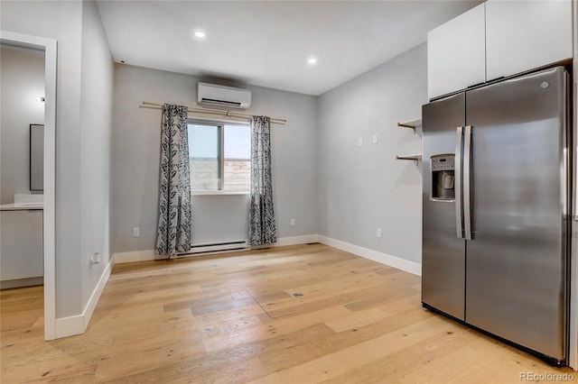 kitchen featuring an AC wall unit, light wood-style flooring, white cabinets, stainless steel fridge with ice dispenser, and baseboards