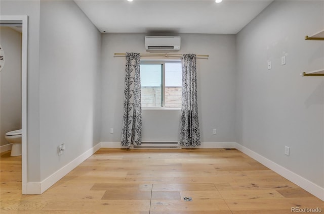 empty room with a baseboard heating unit, light wood-style flooring, baseboards, and a wall mounted air conditioner