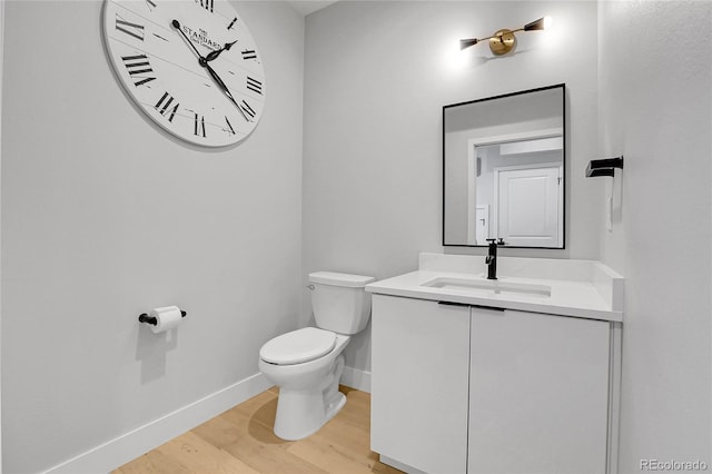 half bath with vanity, toilet, wood finished floors, and baseboards