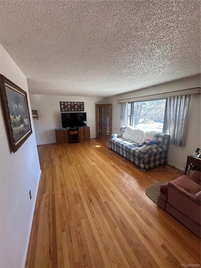 unfurnished living room with baseboards, light wood-type flooring, and a textured ceiling