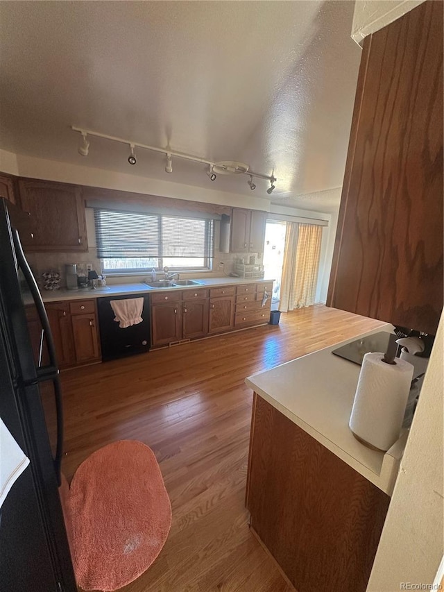 kitchen featuring wood finished floors, a sink, black appliances, light countertops, and tasteful backsplash