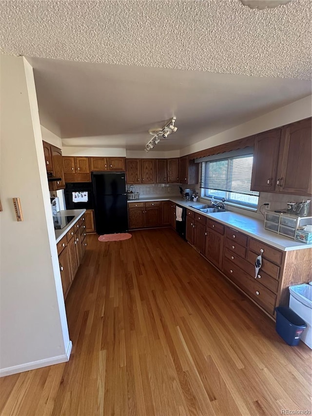 kitchen with wood finished floors, a sink, decorative backsplash, black appliances, and light countertops