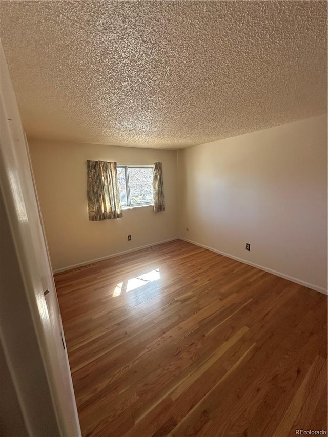 spare room featuring a textured ceiling, baseboards, and wood finished floors