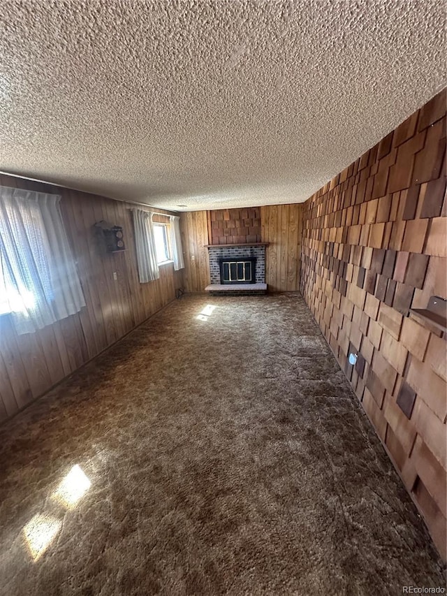 unfurnished living room with carpet flooring, a textured ceiling, wooden walls, and a glass covered fireplace