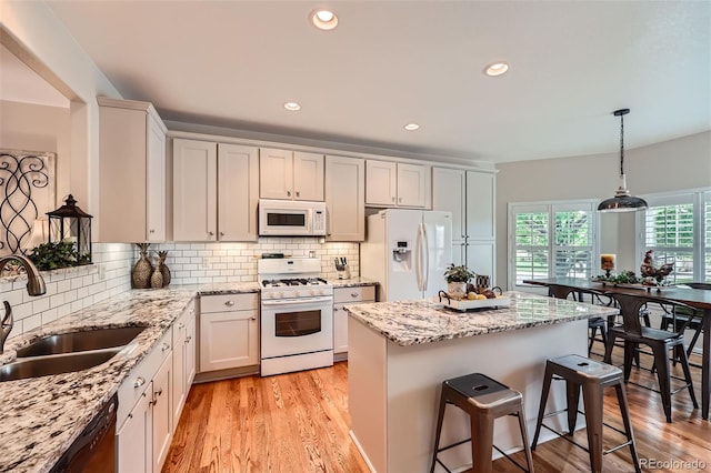 21107 Hawthorne Ln, Parker, CO 80138 - kitchen featuring white appliances, a breakfast bar area, a center island, light wood-type flooring, and decorative backsplash
