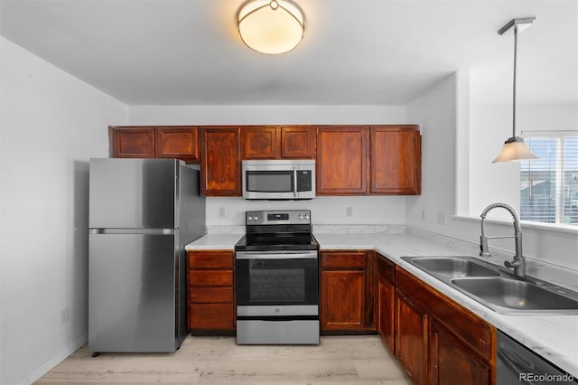 kitchen featuring appliances with stainless steel finishes, hanging light fixtures, sink, and light hardwood / wood-style flooring