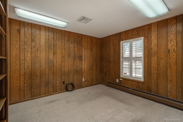 spare room with a baseboard heating unit, carpet floors, wooden walls, and visible vents