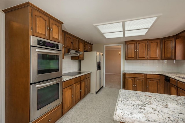 kitchen featuring stainless steel double oven, white fridge with ice dispenser, under cabinet range hood, black electric cooktop, and tasteful backsplash