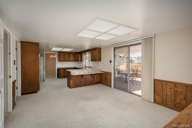 kitchen featuring a wainscoted wall, freestanding refrigerator, a peninsula, light countertops, and light colored carpet