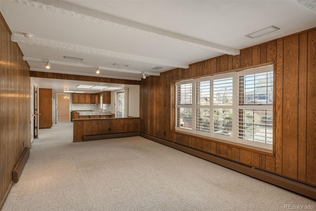 unfurnished living room with a baseboard heating unit, beamed ceiling, light colored carpet, and wood walls