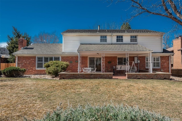 view of front of house featuring a patio area, brick siding, a front lawn, and fence