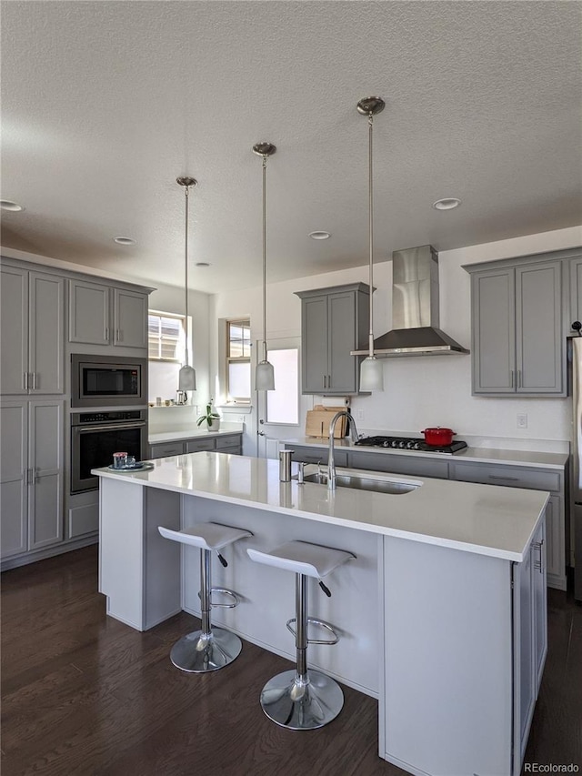 13788 Umatilla Ln, Broomfield, CO 80023 - kitchen featuring wall chimney exhaust hood, stainless steel appliances, gray cabinetry, a textured ceiling, and dark wood finished floors