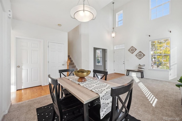 dining area featuring a wealth of natural light, light carpet, and a towering ceiling