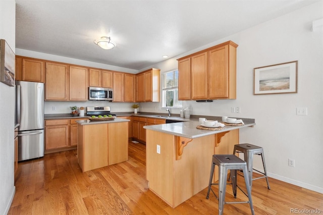 kitchen featuring a kitchen island, appliances with stainless steel finishes, a breakfast bar, light hardwood / wood-style flooring, and sink