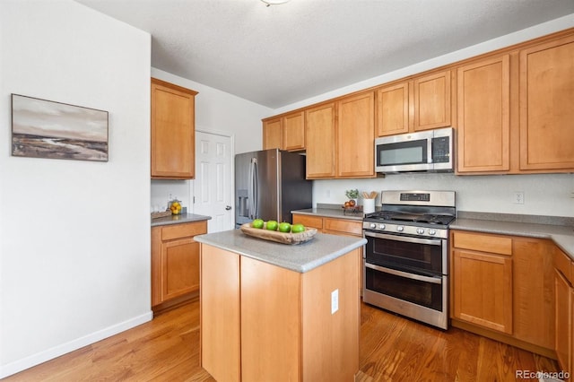 kitchen featuring a textured ceiling, stainless steel appliances, light wood-type flooring, and a kitchen island