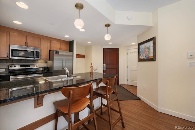 kitchen featuring pendant lighting, a breakfast bar, sink, appliances with stainless steel finishes, and dark hardwood / wood-style flooring