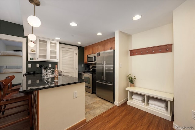 kitchen featuring kitchen peninsula, appliances with stainless steel finishes, a kitchen breakfast bar, light hardwood / wood-style floors, and hanging light fixtures