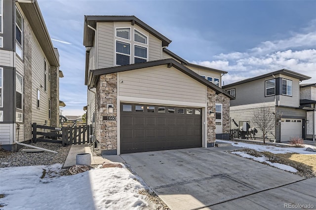 view of front facade with a garage, stone siding, driveway, and fence