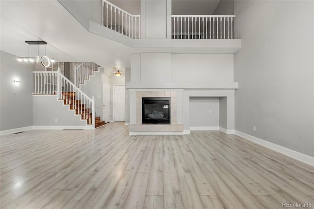 unfurnished living room with light hardwood / wood-style floors, a tile fireplace, a high ceiling, and a chandelier