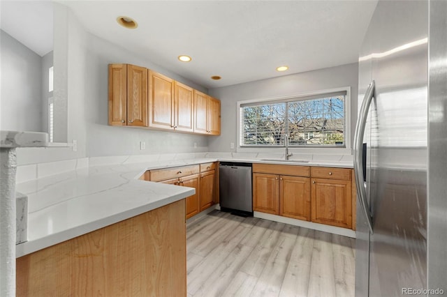 kitchen featuring sink, light wood-type flooring, appliances with stainless steel finishes, light stone counters, and kitchen peninsula