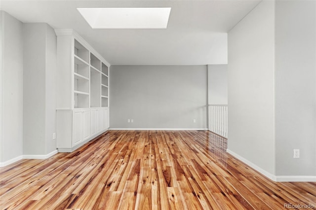 empty room with built in shelves, light wood-type flooring, and a skylight