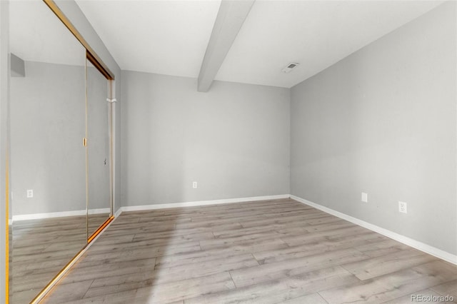 unfurnished bedroom featuring beamed ceiling, light wood-type flooring, and a closet