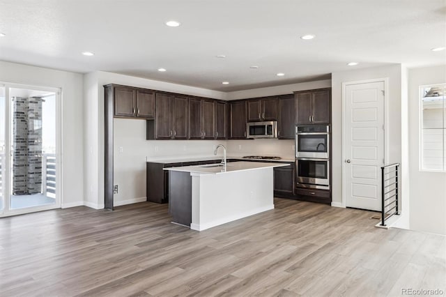 kitchen featuring appliances with stainless steel finishes, light wood-type flooring, a center island with sink, and sink