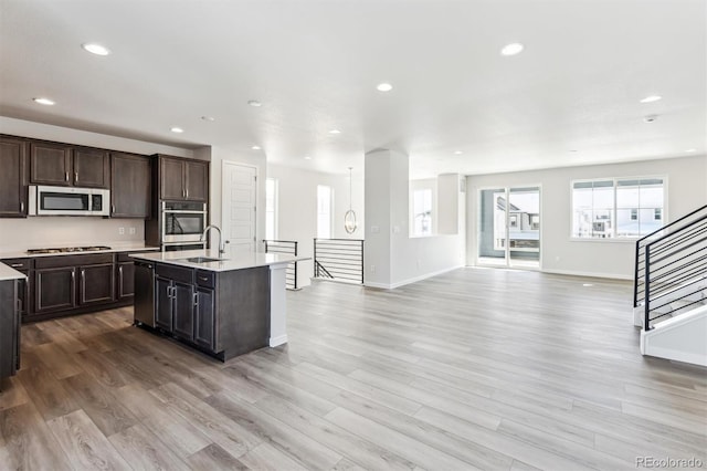 kitchen with sink, light wood-type flooring, stainless steel appliances, and a kitchen island with sink