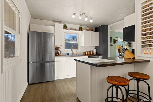 kitchen with dark wood-type flooring, a kitchen bar, stainless steel refrigerator, white cabinets, and sink