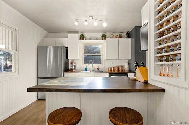 kitchen with sink, a kitchen breakfast bar, wooden counters, and white cabinetry