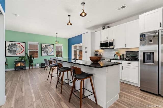 550 S Raleigh St, Denver, CO 80219 - kitchen with appliances with stainless steel finishes, dark countertops, light wood finished floors, decorative backsplash, and white cabinets