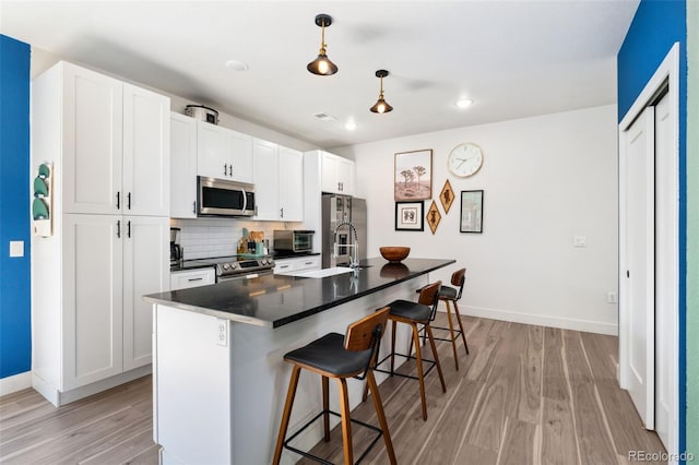 550 S Raleigh St, Denver, CO 80219 - kitchen with stainless steel appliances, a breakfast bar area, dark countertops, light wood-style flooring, and recessed lighting
