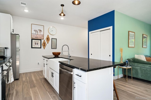 550 S Raleigh St, Denver, CO 80219 - kitchen with stainless steel appliances, light wood finished floors, white cabinets, and an island with sink