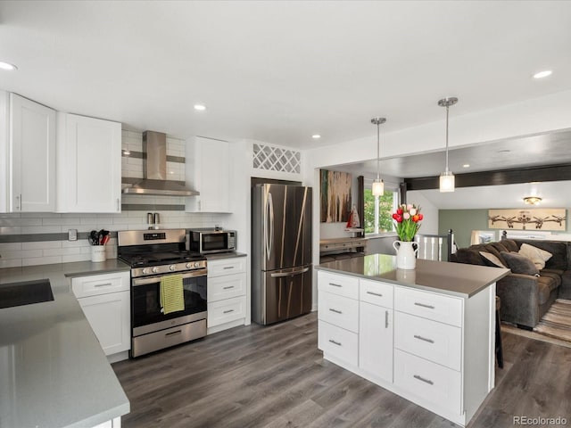 kitchen featuring wall chimney range hood, stainless steel appliances, open floor plan, decorative backsplash, and dark wood finished floors
