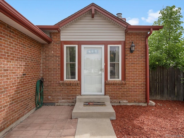 view of exterior entry featuring fence and brick siding