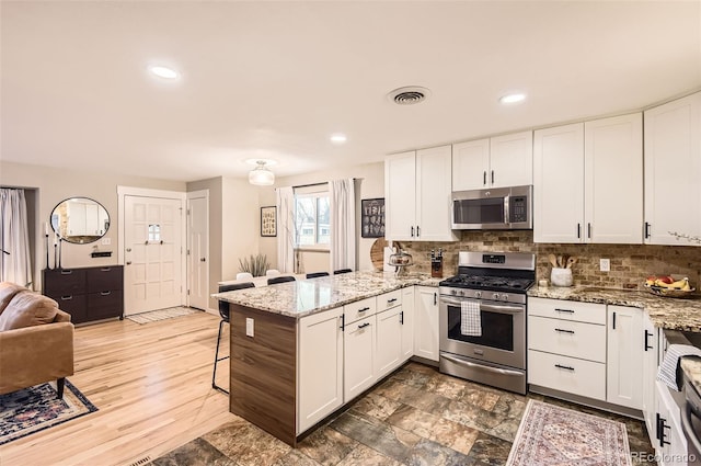 kitchen with white cabinets, stainless steel appliances, a breakfast bar, and a peninsula