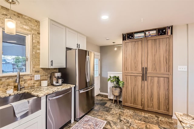 kitchen featuring light stone countertops, white cabinets, a sink, stone finish flooring, and appliances with stainless steel finishes