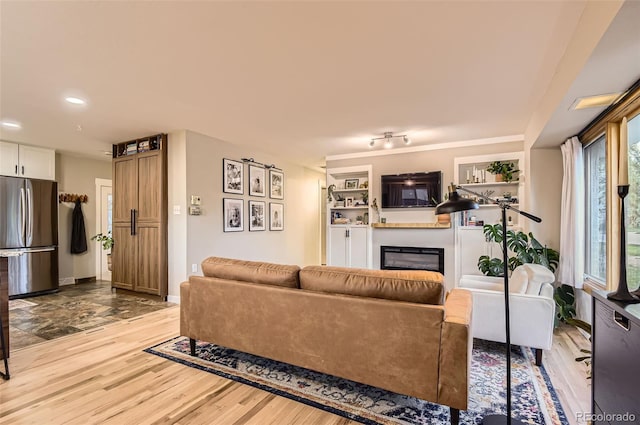 living area with recessed lighting, a glass covered fireplace, and light wood-type flooring