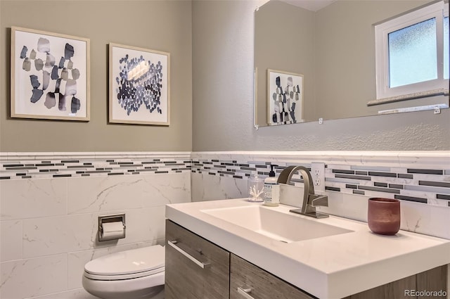 bathroom with tile walls, a wainscoted wall, vanity, and toilet